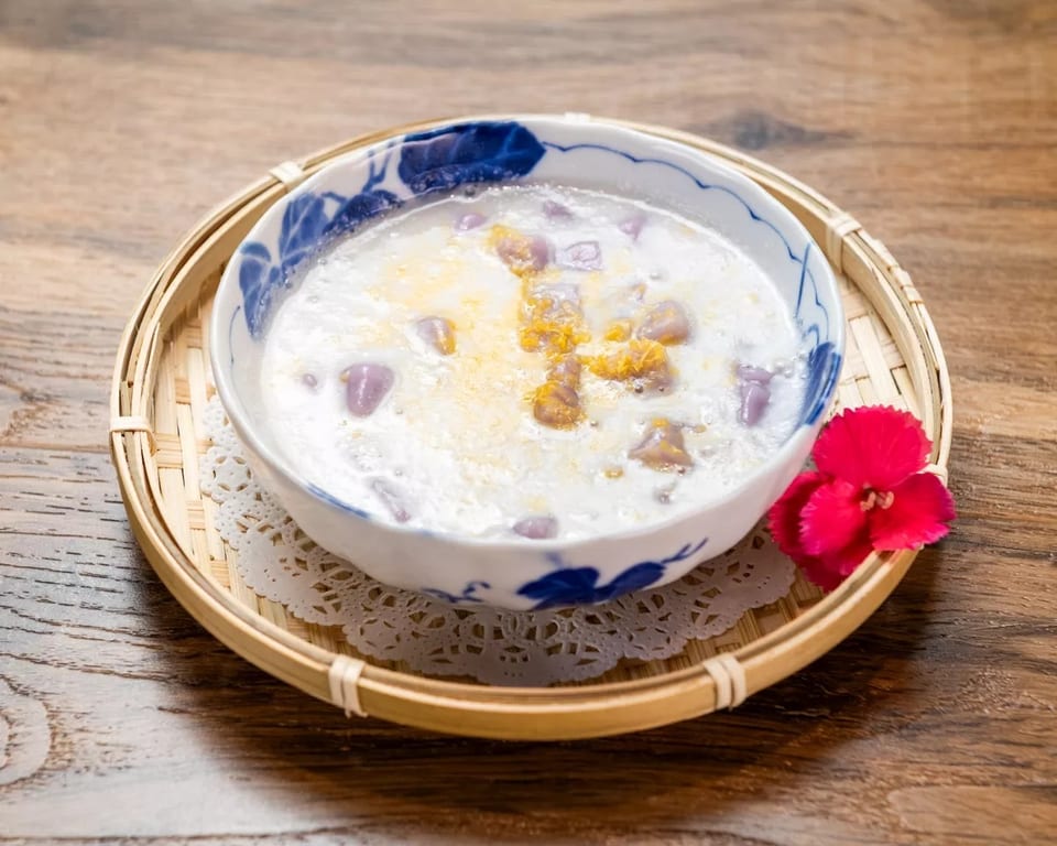 A bowl of taro dessert soup with purple taro chunks and yellow topping, on a bamboo tray.