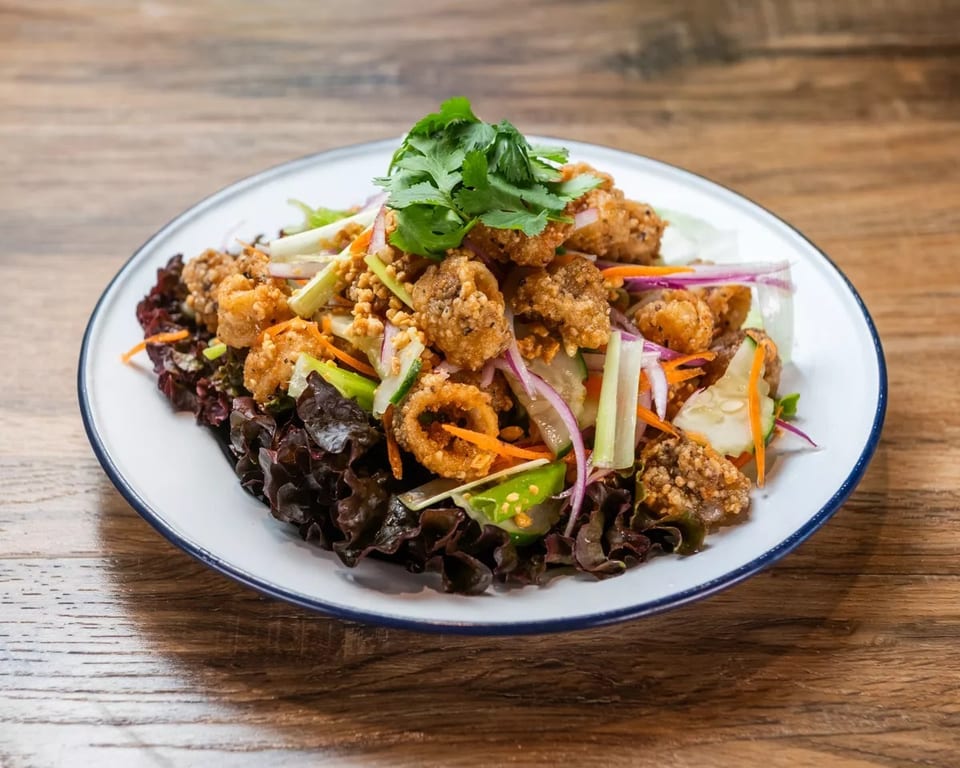 Crispy calamari salad with red lettuce, cucumber, carrots, red onion, and cilantro on a white plate.