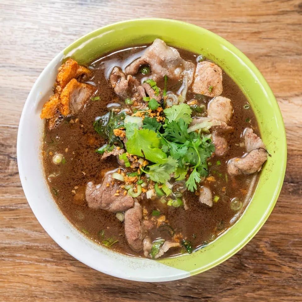 Overhead view of a bowl of Thai boat noodles with beef, meatballs, and cilantro.