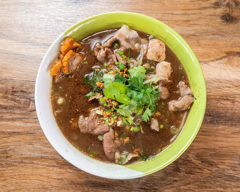 Overhead view of a bowl of Thai boat noodles with beef, meatballs, and cilantro.